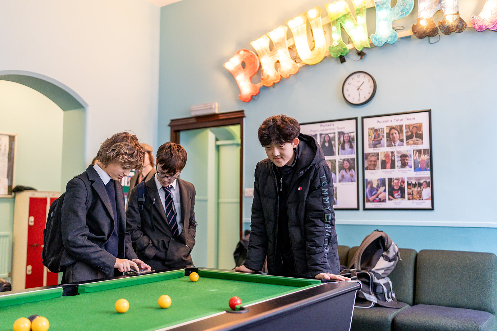 Three boys standing by pool table, in boarding house